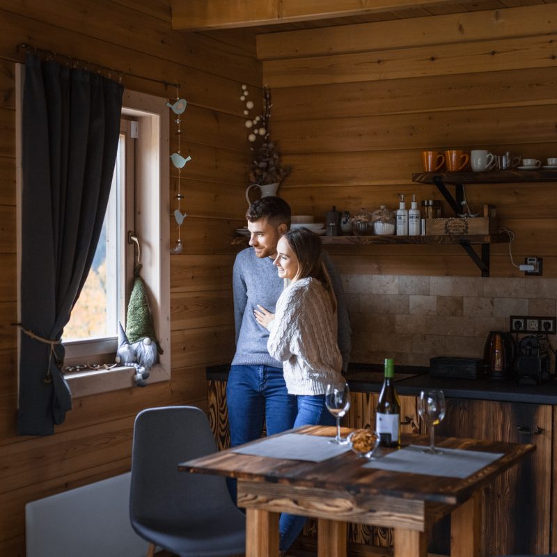 Fiatal pár egymást ölelve nézik a természetet a Chalet konyhai ablakából