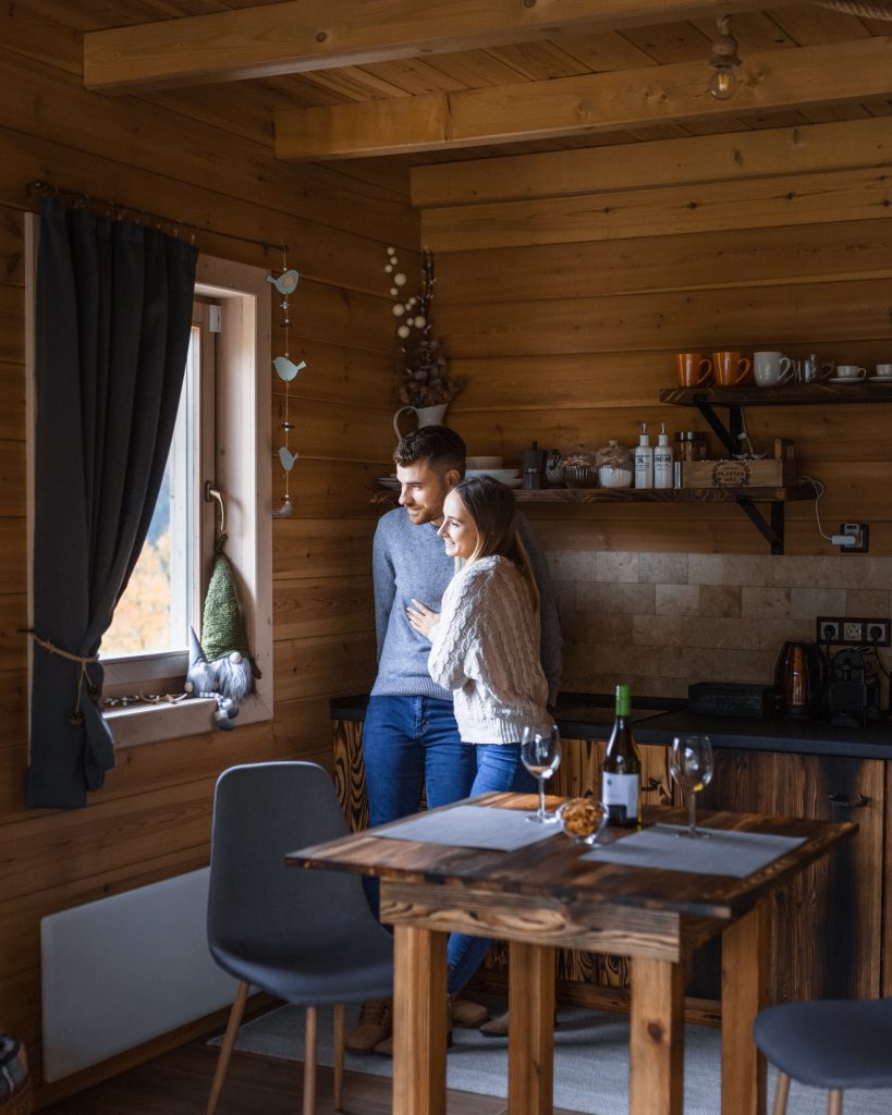 Fiatal pár egymást ölelve nézik a természetet a Chalet konyhai ablakából