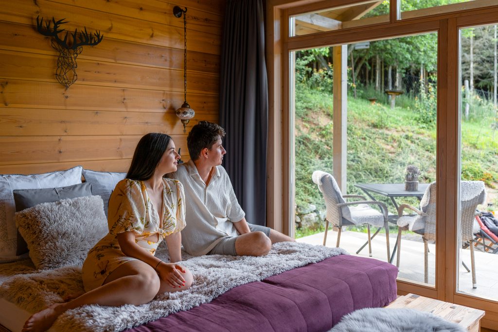 Fiatal pár a Chalet franciaágyán ülnek és a tájat csodálják a panorámaablakokon keresztül