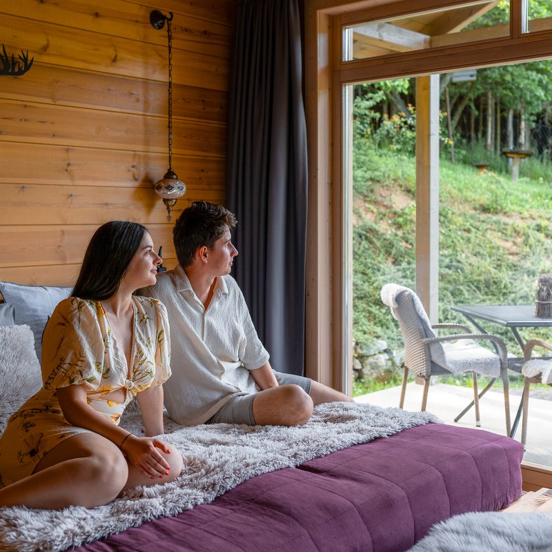 Fiatal pár a Chalet franciaágyán ülnek és a tájat csodálják a panorámaablakokon keresztül